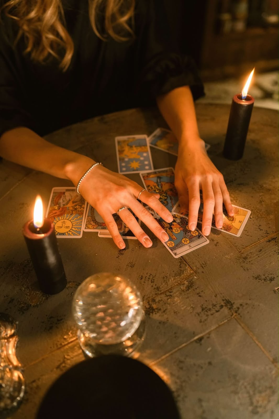 Hands reading tarot cards by candlelight with a crystal ball